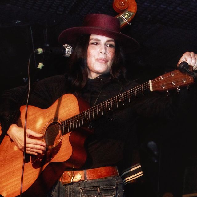 Tomasina Parrott in a black jacket and maroon hat tuning a guitar.
